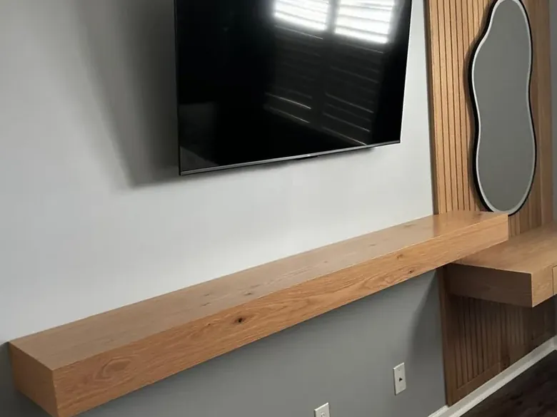 Custom media wall with a thick white oak floating shelf and slat panel behind a wall-mounted TV